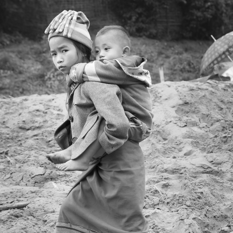 fillette portant sur le dos son petit frère sur le bord de la rivière Nam Ou